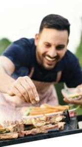 man sprinkling seasoning on grill